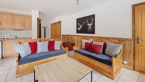 A cozy living area with a wooden sofa set, a small wooden table, and a kitchen in the background.
