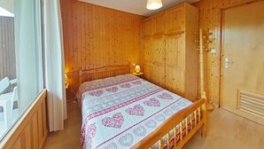 Une chambre avec des murs en bois, un lit recouvert d’une couvre-lit à motifs, une lampe de chevet et une fenêtre avec des rideaux.