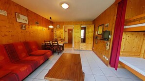 A cozy room with a wooden interior, a sofa, a dining table, and a TV. - Cozy studio in Chinaillon, close to slopes and shops (Le Grand-Bornand)