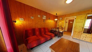 A cozy living room with a red sofa, wooden coffee table, and a dining area with chairs and a table. - Cozy studio in Chinaillon, close to slopes and shops (Le Grand-Bornand)