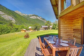 A wooden deck with a table set for dining, overlooking a mountainous landscape.