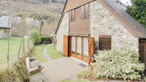 A stone house with a sloped roof, wooden shutters, and a stone wall.