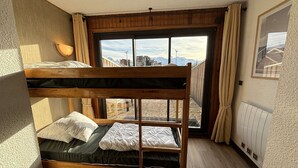 A bunk bed room with a large window, wooden walls, and a radiator.