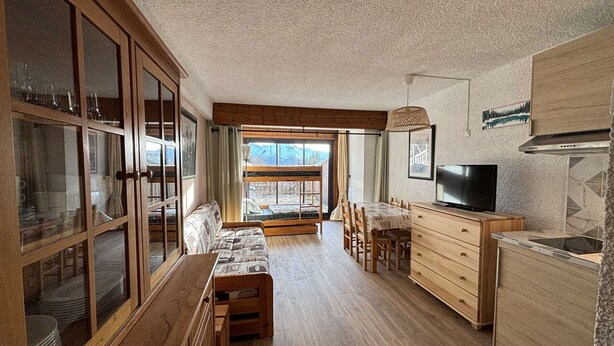 A cozy cabin interior with a wooden dining area, a sofa, a TV, and a kitchen with a stove.