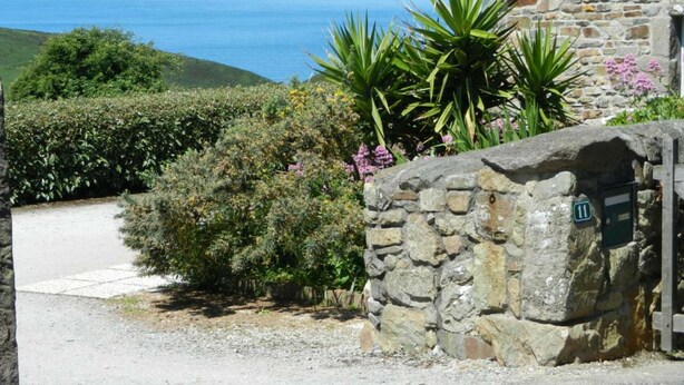 A stone building with a stone wall entrance, a gravel path, and a view of the sea. - Charming stone house with garden and wifi, near the sea (La Hague)
