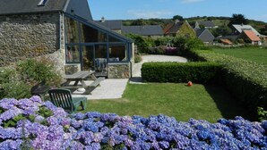 A stone building with a glass extension, a picnic table, and a well-maintained garden with hydrangeas. - Charming stone house with garden and wifi, near the sea (La Hague)
