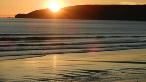 A sunset over a beach with waves approaching the shore. - Charming stone house with garden and wifi, near the sea (La Hague)