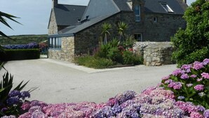 A stone house with a sloped roof and a gravel driveway. - Charming stone house with garden and wifi, near the sea (La Hague)