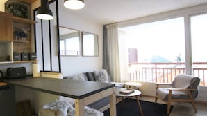 A modern kitchen with a central island, wooden chairs, a small round table, and a view of a balcony with a railing.