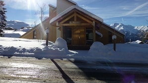 A wooden lodge with a sloped roof, surrounded by snow and mountains.