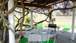 An outdoor dining area with a table set for two, surrounded by white chairs with green cushions.