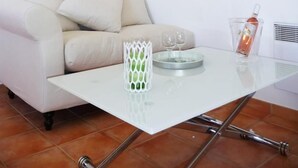A modern living room with a white sofa, a glass coffee table, and two framed botanical prints on the wall.