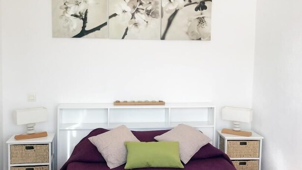 A bedroom with a bed, white headboard, two bedside tables, and a wall-mounted artwork of flowers.