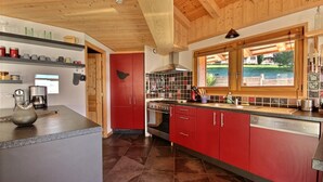 Une cuisine moderne avec des meubles de rangement rouges, une cuisinière et une fenêtre donnant sur un jardin.