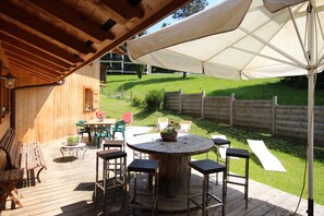 Eine Holzterrasse mit einem runden Tisch und Stühlen, umgeben von einem Holzzaun und einem Rasen.