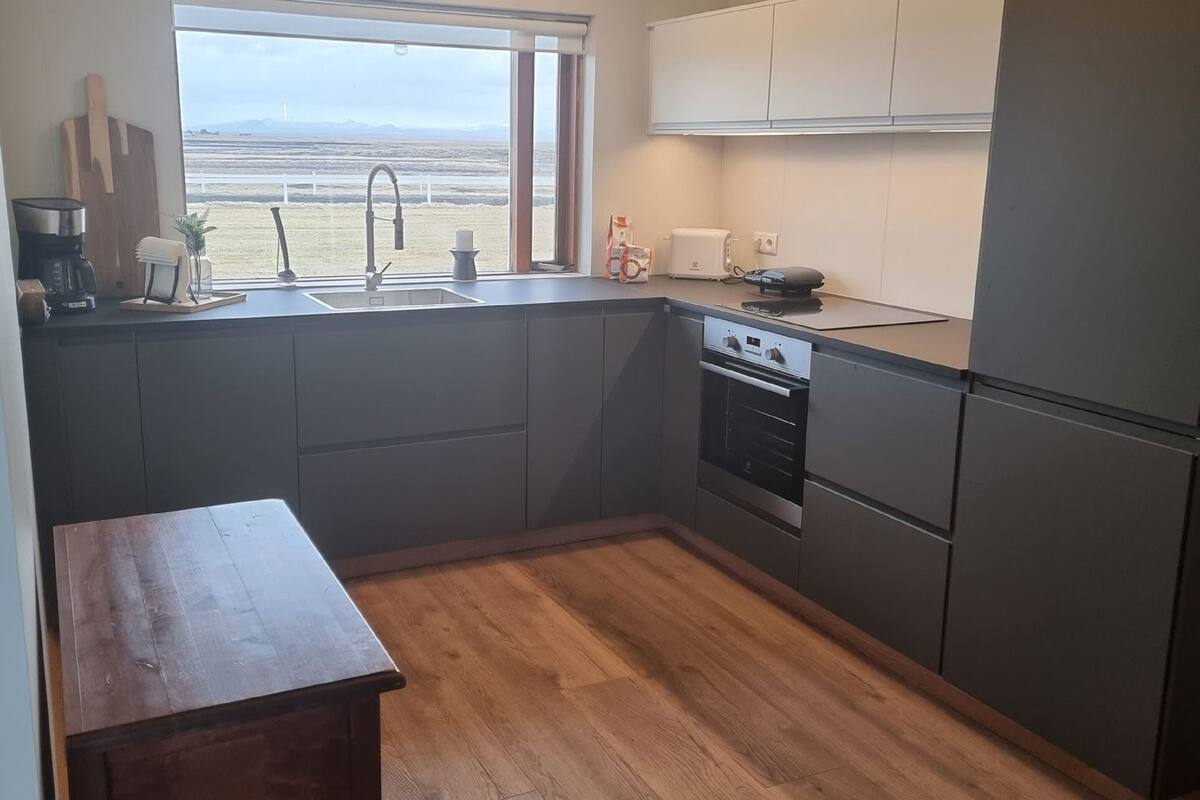 Une cuisine moderne avec une grande fenêtre, des meubles de couleur sombre et une table en bois.
