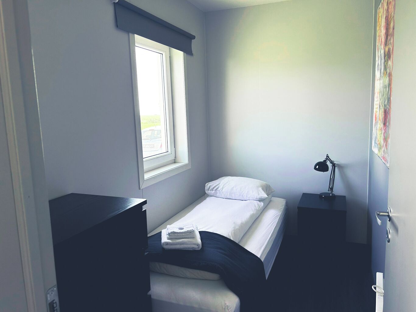 A small, single-bed room with a window, a desk, and a chair.