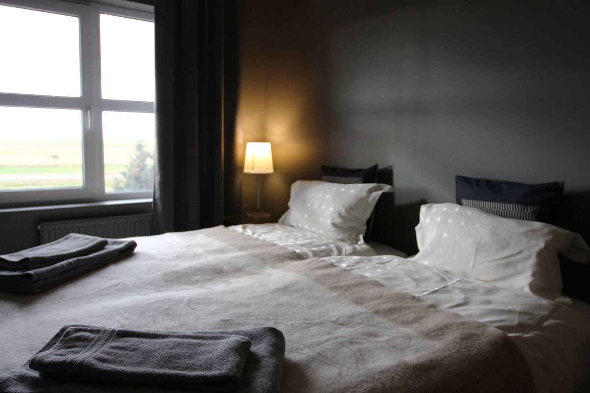 Une chambre d’hôtel avec un grand lit, deux oreillers, une lampe de chevet et une vue sur l’extérieur par une fenêtre.