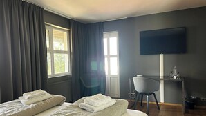 Habitación de hotel con dos camas, un escritorio, una silla y un televisor en la pared.