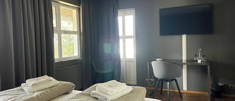 Habitación de hotel con dos camas, un escritorio, una silla y un televisor en la pared.