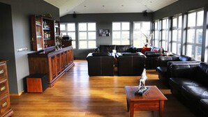Amplia sala de estar con piso de madera, sofá de cuero negro, una mesa de centro de madera y una zona de bar con estantes y botellas.