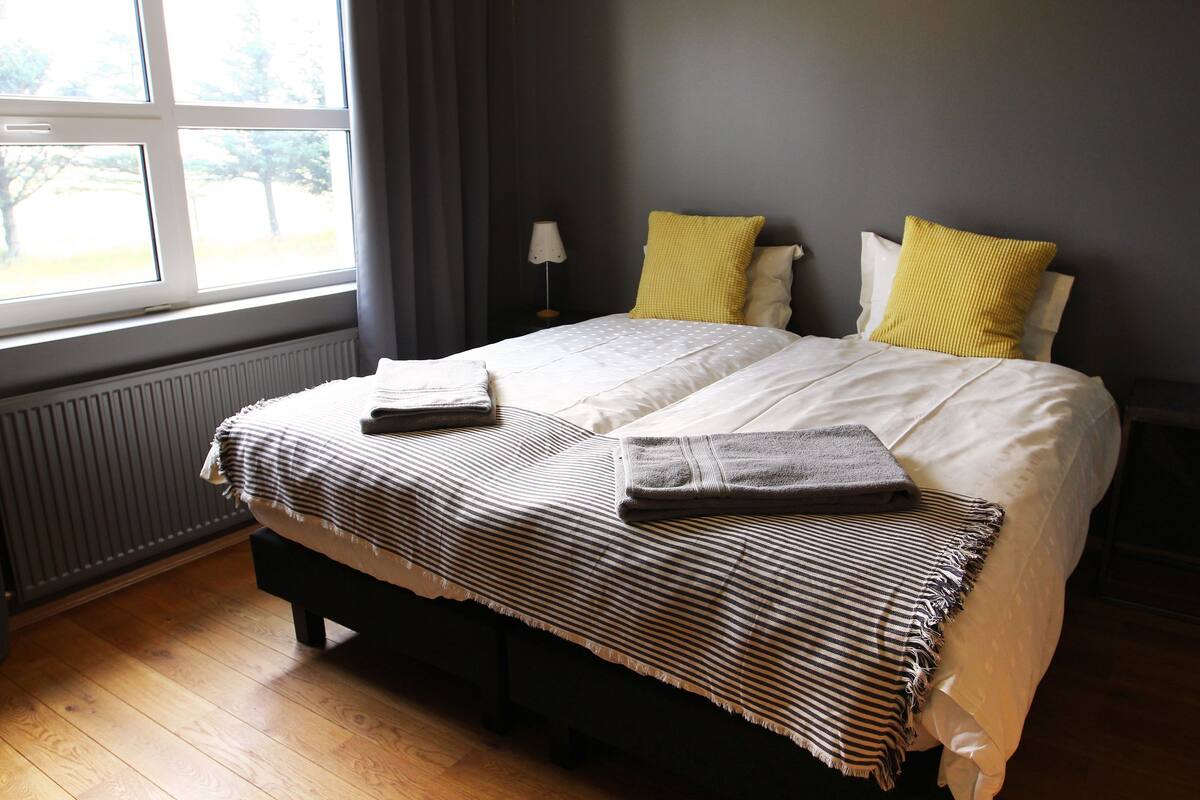 Un lit bien fait, avec une couverture à rayures et deux oreillers, une lampe de chevet et une fenêtre avec des rideaux.
