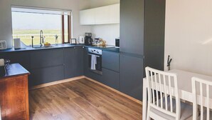 Una cocina moderna con armarios oscuros, encimera de madera, ventana con vistas y un pequeño comedor con sillas blancas.