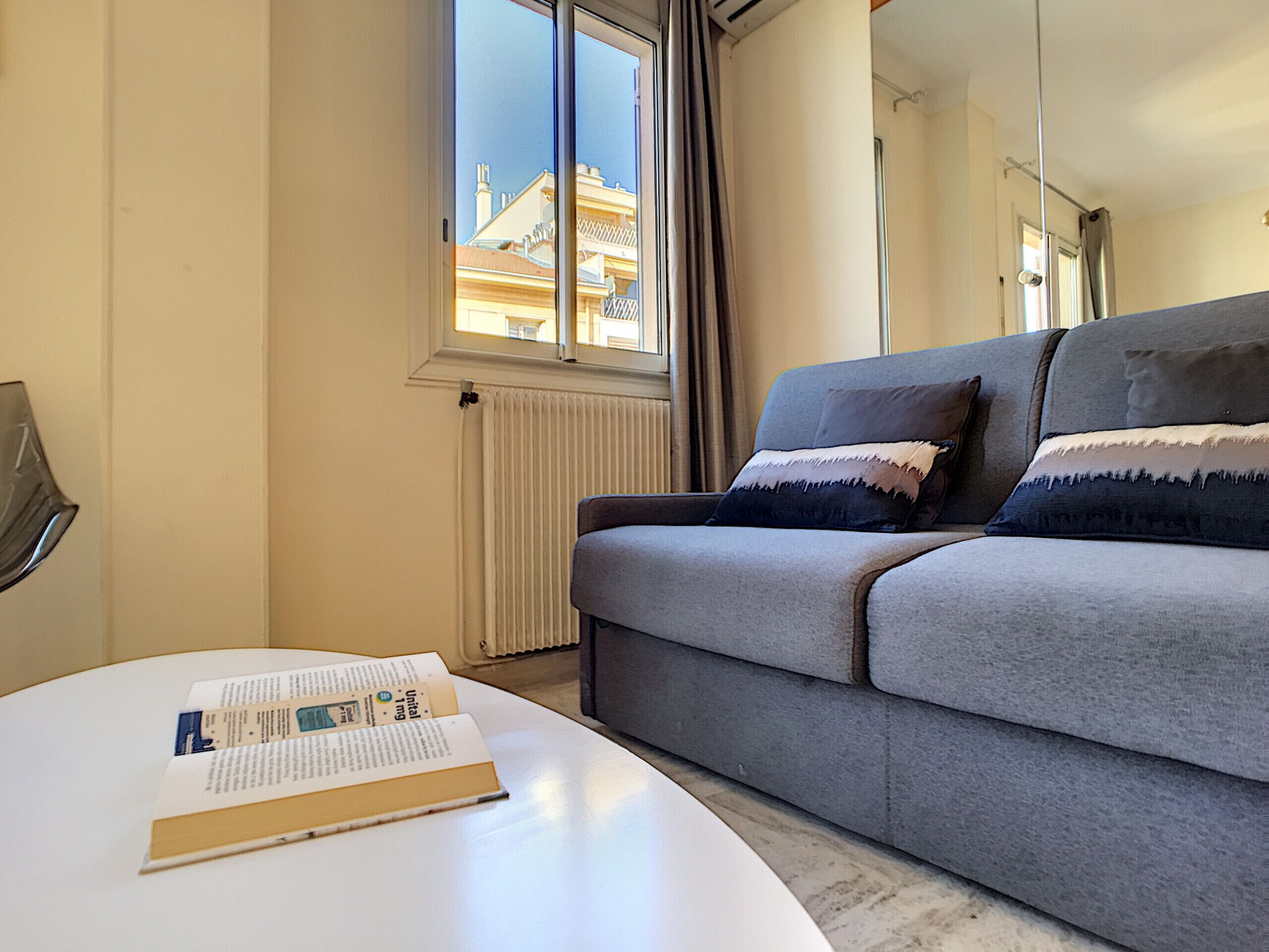 Una sala de estar moderna con un sofá gris, una mesita de centro blanca y una ventana con cortinas.
