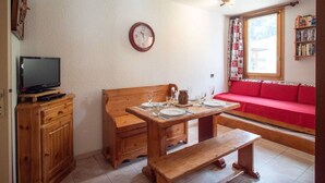 Un accogliente soggiorno con una panca in legno, un tavolo da pranzo per due persone, un divano rosso e una televisione su un mobile in legno.