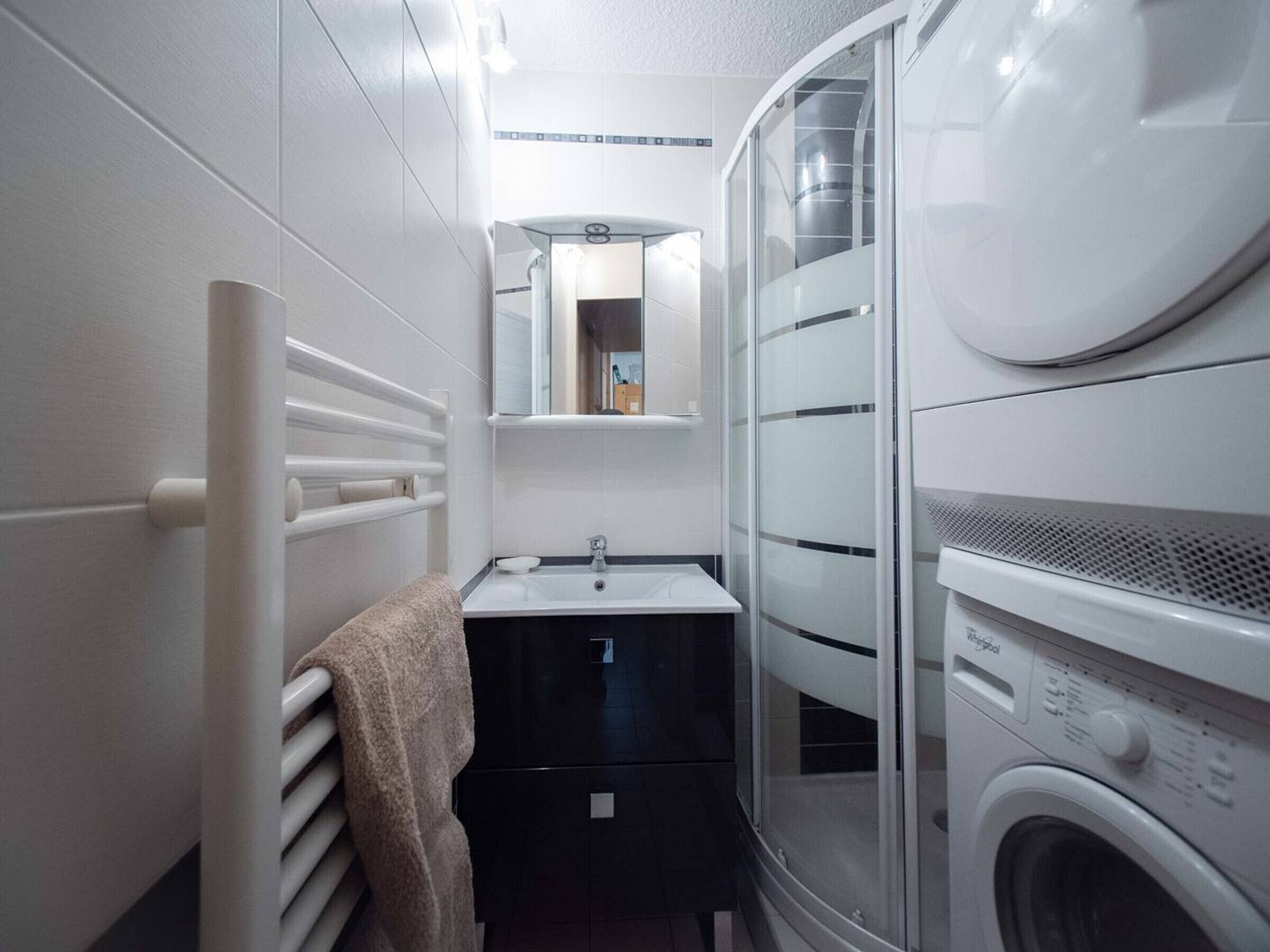 A compact bathroom with a built-in washer and dryer, a towel rack, and a mirror above the sink.