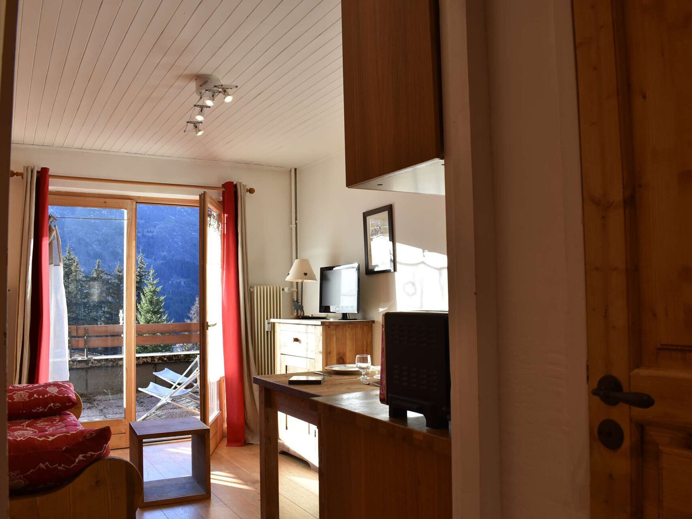 Een kamer met houten plafond, een televisie, een bureau en een raam met uitzicht op bomen en bergen.