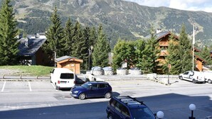 Un parcheggio con diverse auto e un edificio con tetto spiovente, circondato da alberi e montagne sullo sfondo.