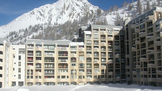 Ein mehrstöckiges Hotel mit Balkonen vor einer verschneiten Berglandschaft.