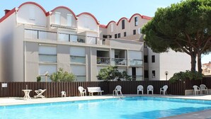 A swimming pool with white lounge chairs and a wooden fence. - Renovated 2-bedroom apartment with pool and parking, sleeps 6 near the beach (Gruissan)
