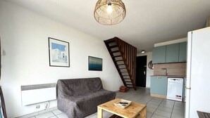 A living room with a sofa, a wooden coffee table, a staircase, and a kitchen area with a dishwasher. - Renovated 2-bedroom apartment with pool and parking, sleeps 6 near the beach (Gruissan)