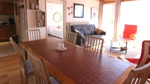 A dining area with a wooden table and chairs, a kitchen in the background, and a living room with a sofa and a red chair. - 3-room apartment, 6 pers, 70m², Vieil Alpe, Alpe d'Huez, pets OK (Huez)