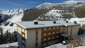 A multi-story building with a flat roof, surrounded by snow-covered mountains and trees. - 3-room apartment, 6 pers, 70m², Vieil Alpe, Alpe d'Huez, pets OK (Huez)