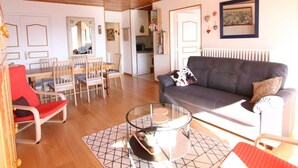A spacious living room with a wooden ceiling, a grey sofa, a glass coffee table, and a dining area with wooden chairs and a red bench. - 3-room apartment, 6 pers, 70m², Vieil Alpe, Alpe d'Huez, pets OK (Huez)