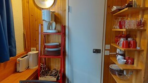 Eine kleine Küche mit Holzwänden, einem weißen Kühlschrank und Regalen mit Geschirr und Gläsern.
