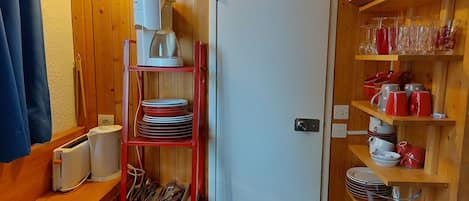 A compact kitchen with wooden walls, a white refrigerator, and shelves with dishes and glasses.