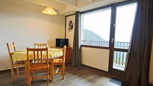 Un área de comedor con una mesa y sillas, un televisor y un balcón con vistas.