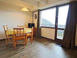 A dining area with a table and chairs, a television, and a balcony with a view.