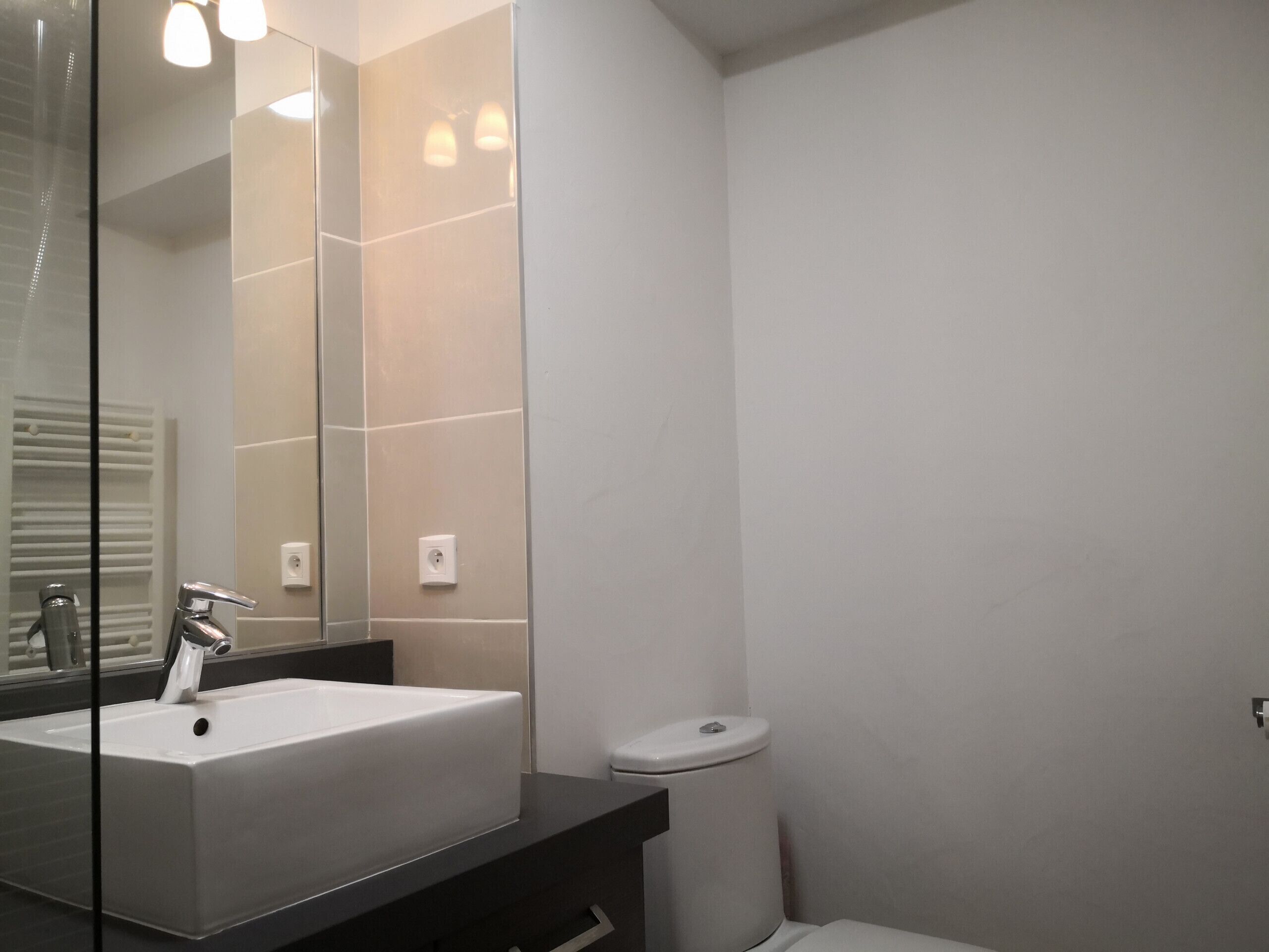 A modern bathroom with a large mirror, a white sink, and a toilet.