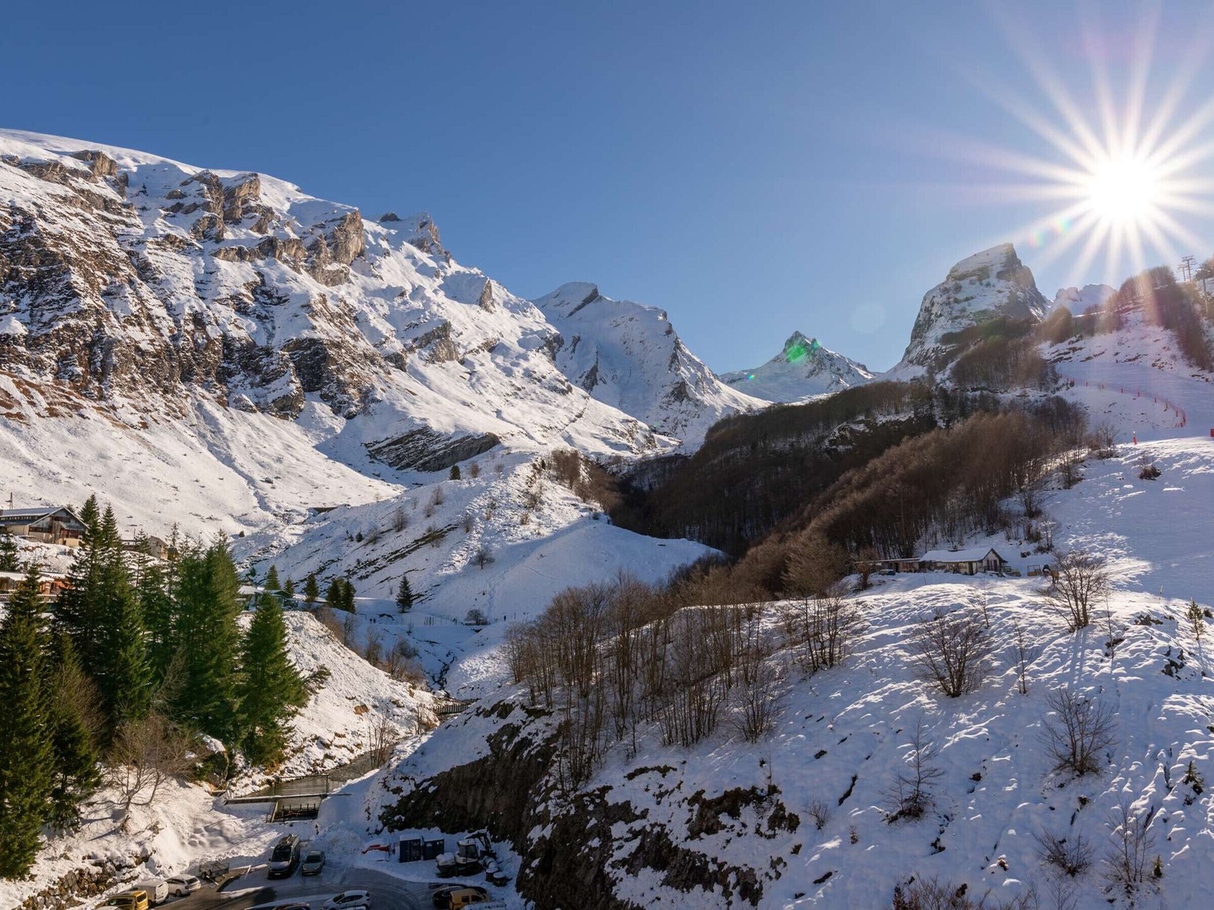 A mountainous landscape with snow-covered peaks, a clear sky, and a bright sun.