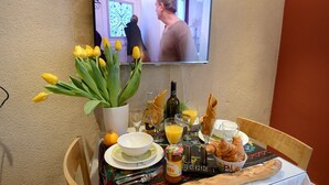 Ett frukostbord med en flaska apelsinjuice, croissanter, en korg med croissanter, en flaska ketchup och en skål med flingor.