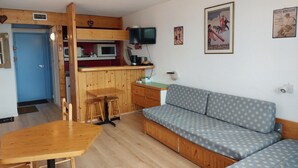 En kompakt opholdsstue med tekøkken, sofa, spisebord og fjernsyn.