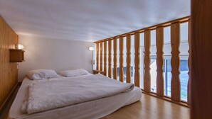 A bedroom with a wooden bed, a nightstand, and a window with a wooden railing.