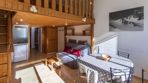 A cozy cabin with a dining area, a kitchen, and a bedroom with a view of a snowy mountain.