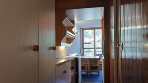 A kitchen with wooden cabinets, a built-in shelf, and a window with a view of trees.