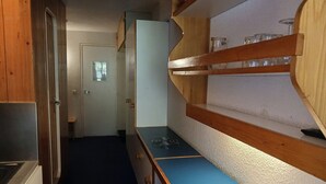 A narrow hallway with a kitchenette area featuring a stove, a sink, and a wooden shelf with jars.